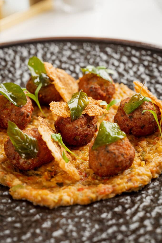 Fine dining presentation of Cumin Meatballs served over a rich Roasted Eggplant & Tomato Choka base, garnished with a Parmesan Tuile and fresh Mint Yogurt at 277 Restaurant in Trinidad