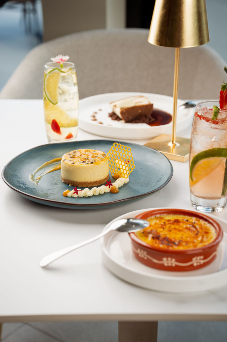 An elegant dessert spread featuring Passion Fruit Cheesecake with digestive crunch and sugar tuile, a burnt sugar Crème Brûlée, and two refreshing cocktails, available at 277 Restaurant in Trinidad